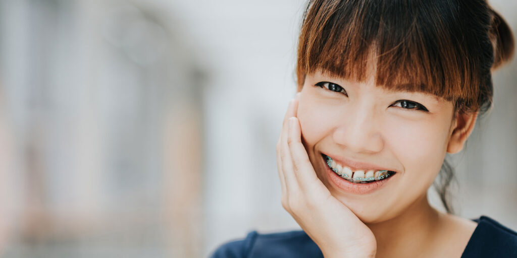 younger women patient with braces smiling outside of the dental practice