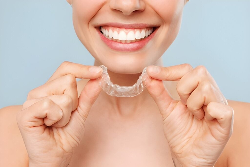 Woman smiling and holding Invisalign clear aligners for teeth straightening.