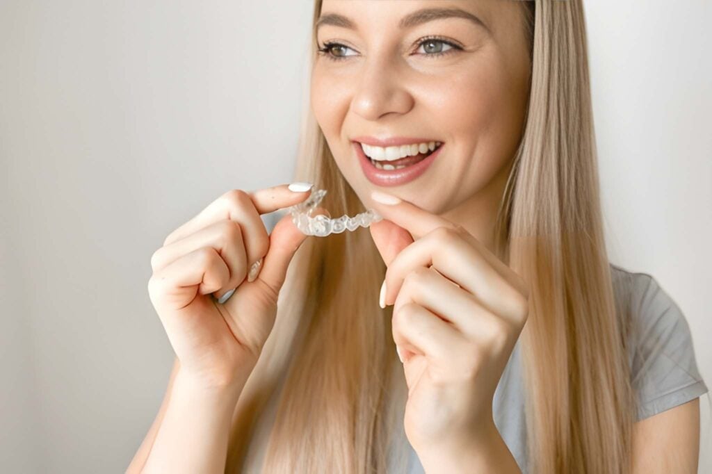 Woman smiling and holding clear aligners, orthodontic treatment options in Woodland Hills, CA.